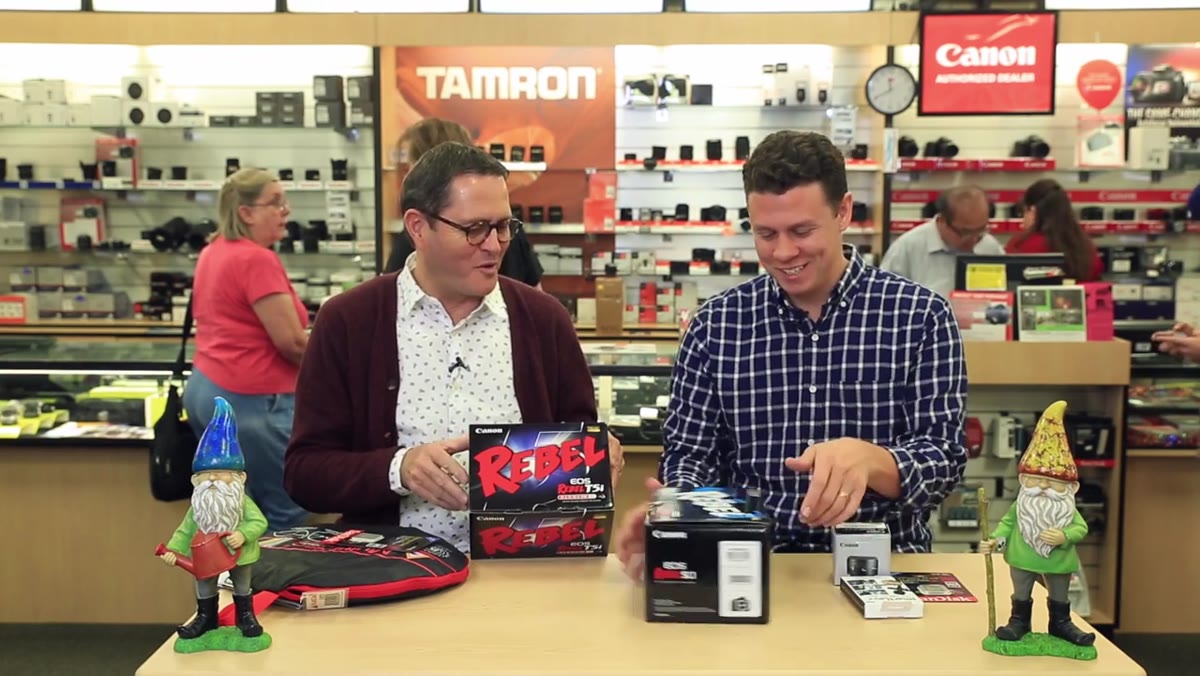 Both hosts comparing Canon Rebel camera bodies on a store counter