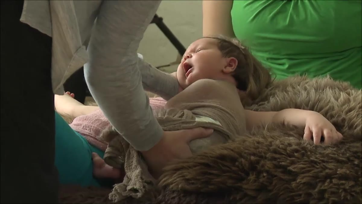 Photographer waiting with hands on swaddled newborn before lifting