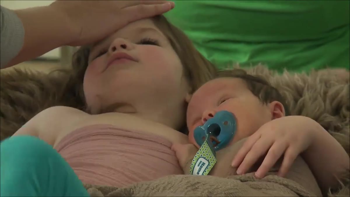 Pillow placed behind sibling&rsquo;s head to bring chin forward toward baby